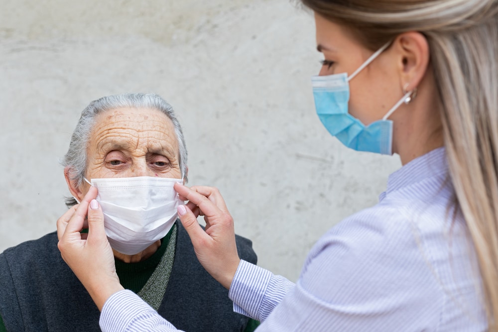 Nurse putting on surgical mask on elderly ill woman - coronavirus protective protocol